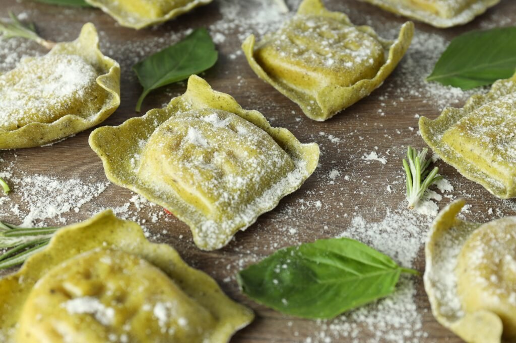 Raw ravioli with flour and basil on wooden background